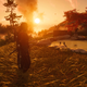Jin Sakai standing in a field at sunset in Ghost of Tsushima while two PS5 screenshot icons are in the upper right hand corner